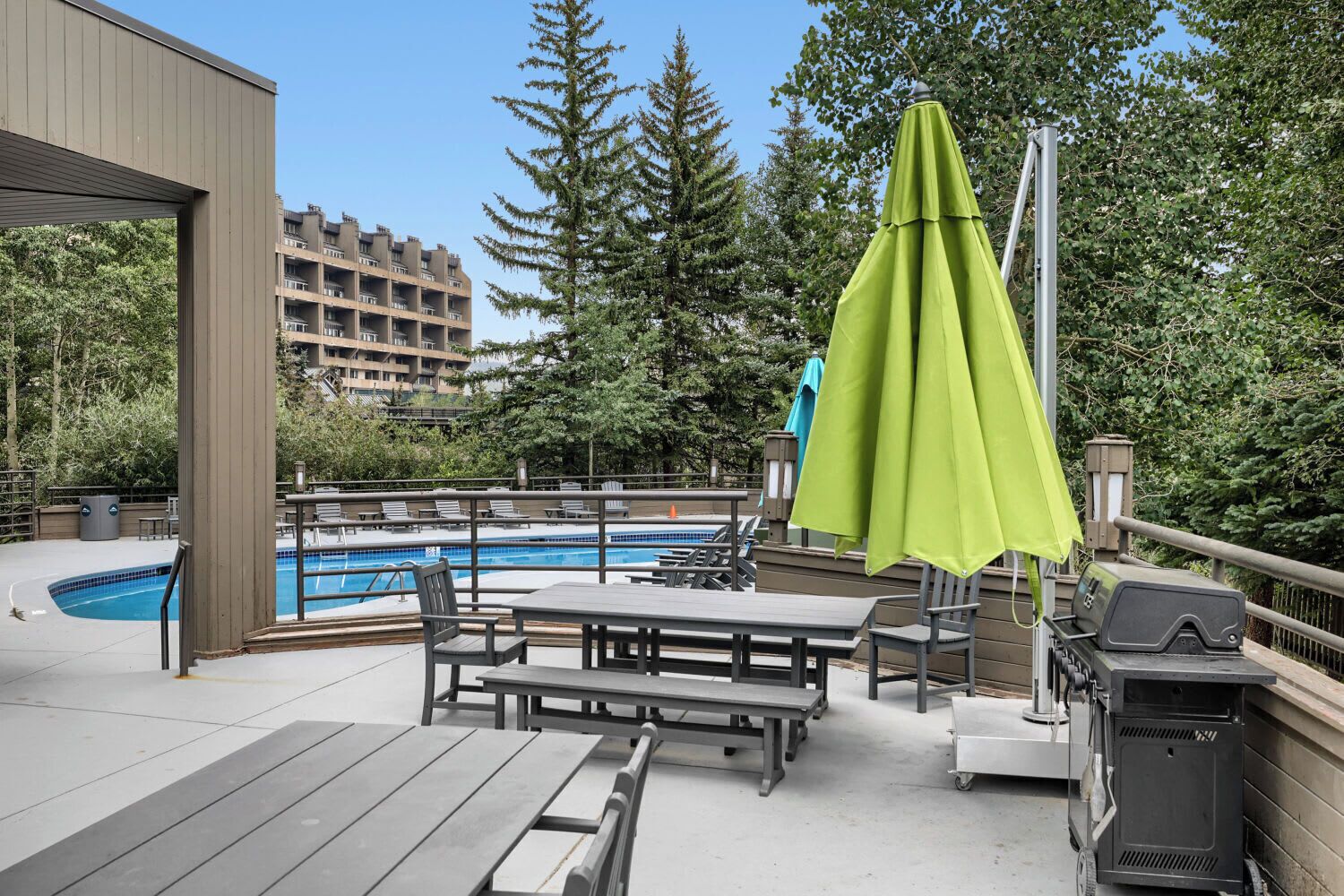 Un área de piscina al aire libre con terraza de madera, sillones de descanso y una parrilla.
