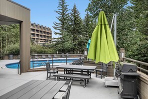 Un área de piscina al aire libre con terraza de madera, sillones de descanso y una parrilla.