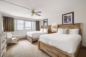 Habitación de hotel con dos camas, un escritorio, una silla, un ventilador de techo y una ventana con cortinas.