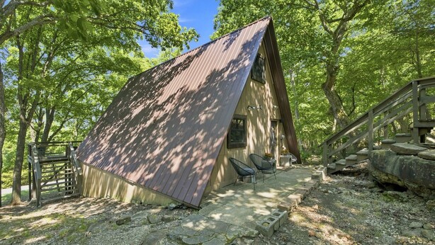 A small cabin with a sloped roof, a porch with two chairs, and a wooden staircase leading up to it.