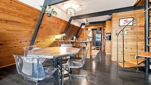 A dining area with a round table, clear chairs, and a wooden ceiling.