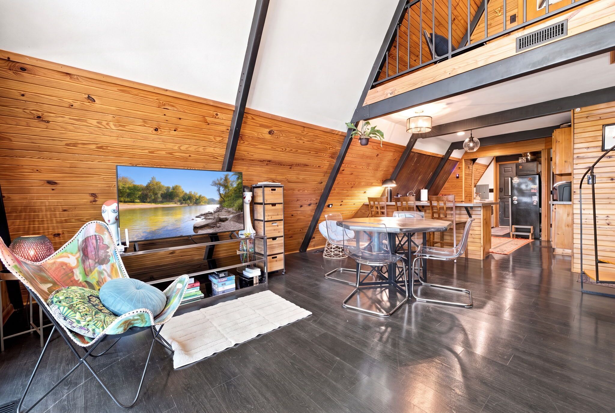 A modern loft-style room with a large TV, a dining table, and a cozy seating area.