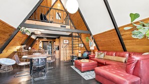 A spacious loft with a high ceiling, a dining area, a red leather sofa, and a kitchen.
