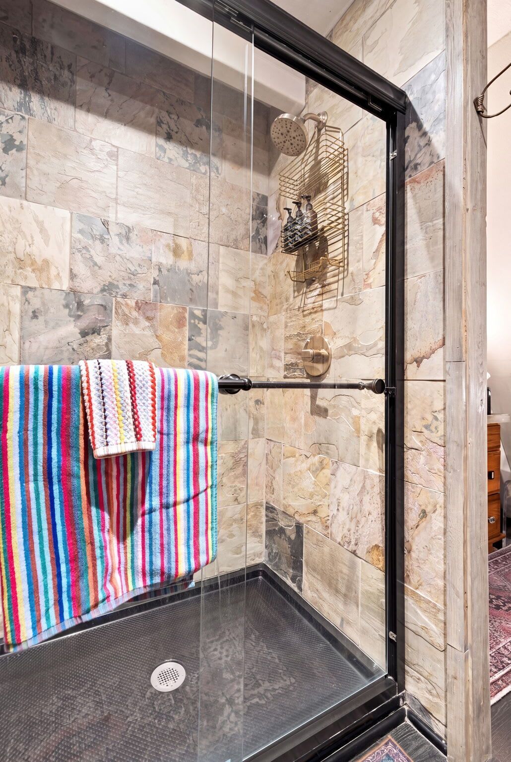 A glass-enclosed shower with a towel rack, marble tiles, and a showerhead.