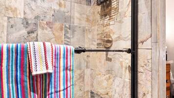 A glass-enclosed shower with a towel rack, marble tiles, and a showerhead.
