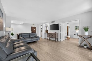 A modern living room with a grey leather sofa, a wooden coffee table, and a flat-screen TV mounted on the wall. - The Drift On The Ocean (Fort Lauderdale)