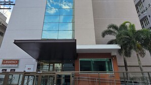 Um edifício de vários andares com fachada de vidro destacada, entrada coberta e calçada quadriculada à frente.