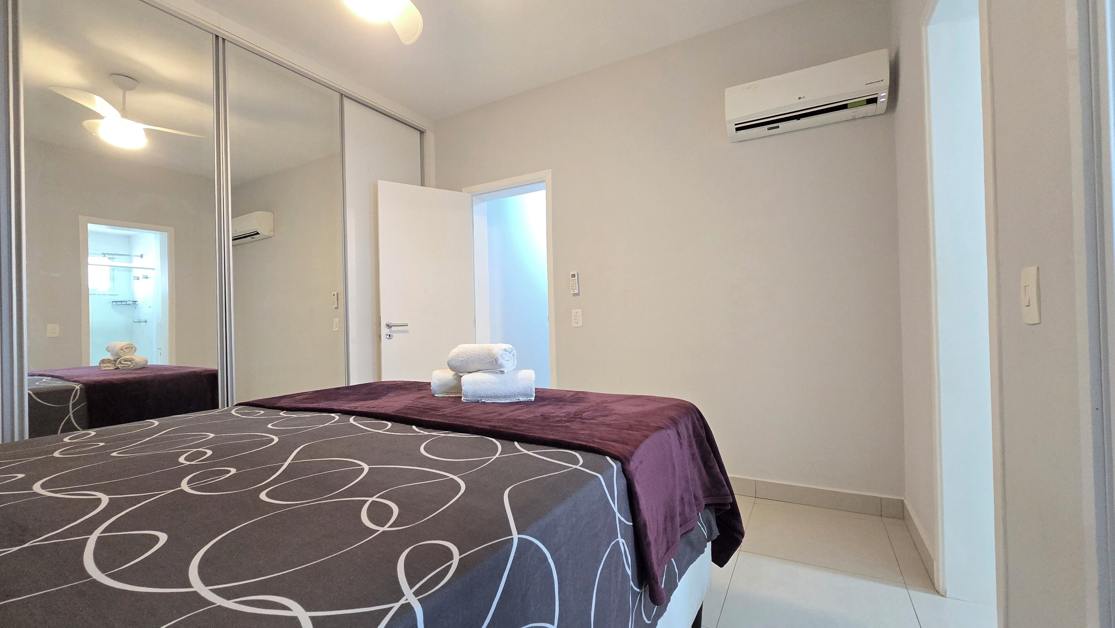 Quarto de hotel com cama, espelho, ar condicionado e porta para um banheiro.