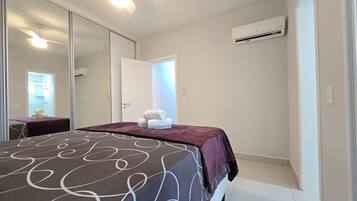 Quarto de hotel com cama, espelho, ar condicionado e porta para um banheiro.
