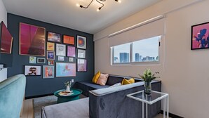 A modern living room with a grey sofa, a coffee table, and a city view through a large window. - Two Roma Norte Condos with City Views & Workspace (Ciudad de México)