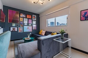 Ein modernes Wohnzimmer mit grauem Sofa, einem Couchtisch und Blick auf die Stadt durch ein großes Fenster.