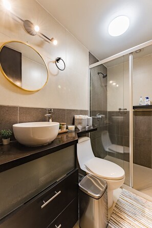 Een moderne badkamer met een groot ovaal wastafel, toilet, douchecabine en een spiegel met ingebouwde verlichting.