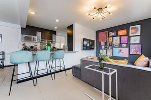 A modern kitchen with a central island, bar stools, and a dining area with a sofa and coffee table. - Two Roma Norte Condos with City Views & Workspace (Ciudad de México)