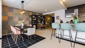 A modern kitchen with a dining area, featuring a black and white checkered rug, a dining table with chairs, a bar area with stools, and a stone wall backsplash. - Two Roma Norte Condos with City Views & Workspace (Ciudad de México)