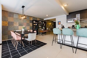 Eine moderne Küche mit Essbereich, mit einem schwarz-weißen Schachbrettteppich, einem Esstisch mit Stühlen, einer Bar mit Hockern und einer Wandverkleidung aus Naturstein.