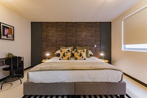 Una camera da letto moderna con una parete in mattoni a contrasto, un letto con cuscini a motivi geometrici, lampade da comodino e una scrivania con una sedia.