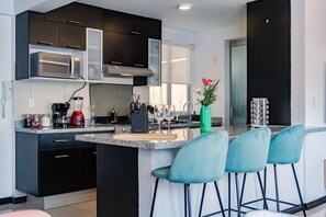 A modern kitchen with dark cabinets, a built-in microwave, a coffee maker, and a wine glass on the counter. - Two Roma Norte Condos with City Views & Workspace (Ciudad de México)