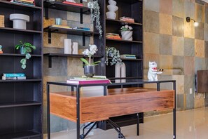 Un intérieur moderne avec un bureau en bois, des étagères en métal noir ornées de livres et d’objets décoratifs, et un mur à carreaux.