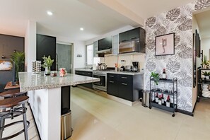 A modern kitchen with a central island, black cabinets, stainless steel appliances, and a decorative wall with a floral pattern. - Two Roma Norte Condos with City Views & Workspace (Ciudad de México)