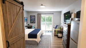 Una camera da letto con un letto, una cassettiera, una televisione e una porta scorrevole che dà su un balcone.