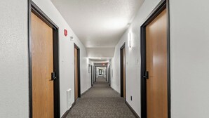 Un corridoio di un hotel con pavimenti rivestiti di moquette, porte in legno e lampade.