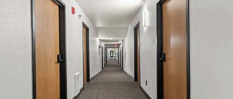 A hotel hallway with carpeted floors, wooden doors, and light fixtures.