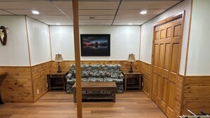 Una habitación con paneles de madera, un sofá, dos lámparas, una mesa y una mesa de futbolín.