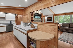 A modern kitchen with wooden accents, a dining area with a round table, and a living room with a leather sofa.
