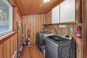 Een wasserette met een wasmachine, droger en diverse schoonmaakspullen.