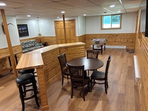 A wooden-floored room with a bar area, seating, and a foosball table.