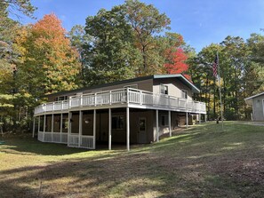 A two-story house with a porch and a balcony, surrounded by trees with autumn foliage.