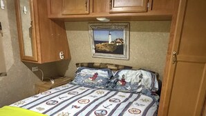 A bedroom with a bed, a wooden wardrobe, a mirror, and a framed picture on the wall.