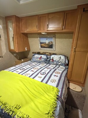 A bedroom with a bed, a wooden wardrobe, a mirror, and a framed picture on the wall.