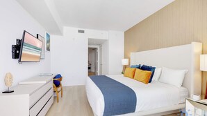 A modern hotel room with a large bed, bedside lamps, a desk with a computer, and a chair. - 2BR Ocean Views & Modern Comfort (Hollywood)