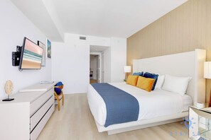A modern hotel room with a large bed, bedside lamps, a desk with a computer, and a chair. - 2BR Ocean Views & Modern Comfort (Hollywood)