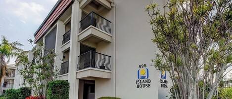 Un edificio residencial de varios pisos con balcones, un cartel que dice 'Island House' y follaje circundante.