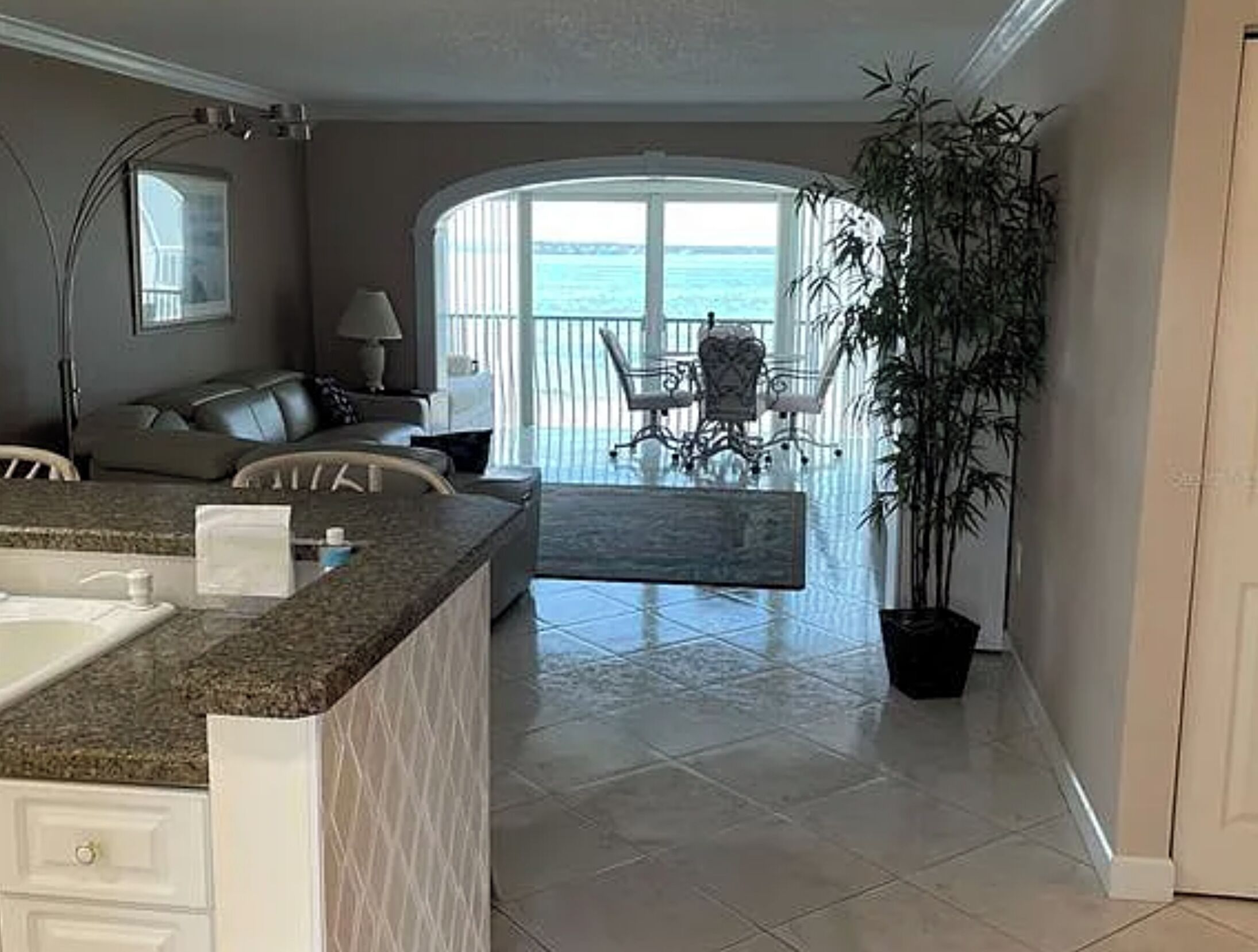 A modern kitchen with a granite countertop, a dining area with a table and chairs, and a view of the ocean through large windows.