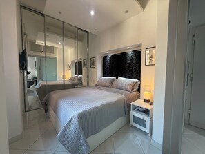 A modern bedroom with a large bed, a bedside table with a lamp, and a mirror. - Sisto Suite - Charming 1-bedroom apartment with AC in vibrant Roma (Roma)