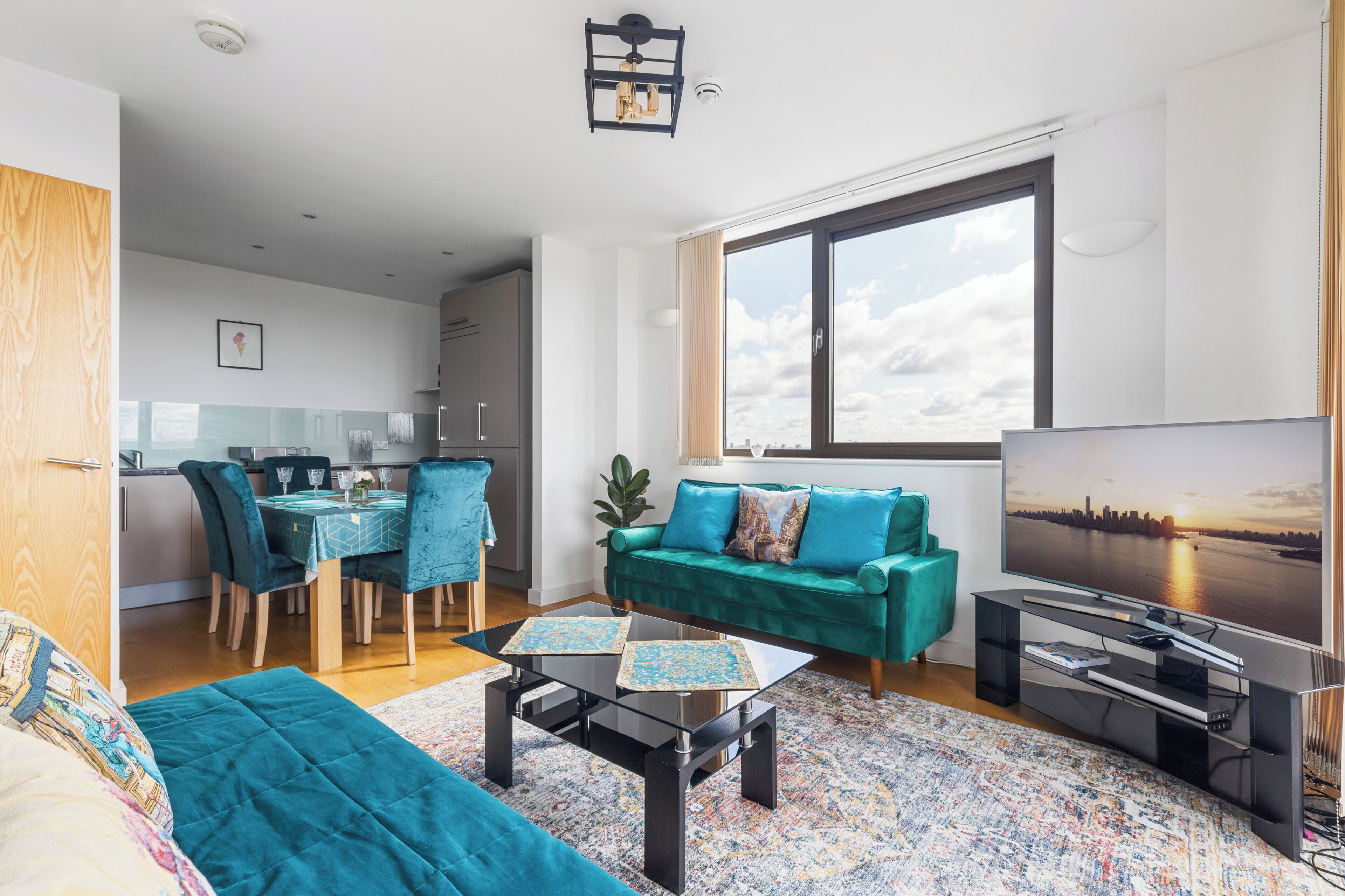 En moderne stue med en tealgrøn sofa, et sofabord og et fjernsyn, der viser et bybillede.