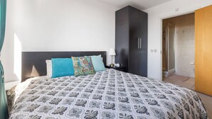 Quarto com cama, mesa de cabeceira, luminária, guarda-roupa e porta do banheiro.