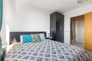 Ein Schlafzimmer mit Bett, Nachttisch, Lampe, Kleiderschrank und einer Badezimmertür.