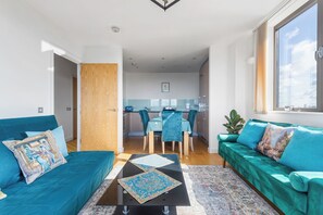 A modern living room with teal sofas, a coffee table, and a dining area with chairs and a table. - Apartment with Beautiful View one stop to Central London (London)