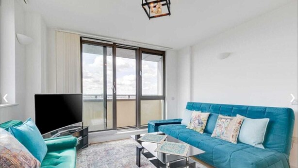 Uma sala de estar moderna com uma janela grande, um sofá azul, uma TV e uma mesa de centro.