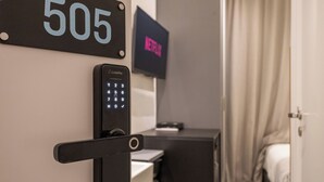 Ein Hotelzimmer mit digitalem Schlüssellock, einem Schild mit der Nummer 505 und einem Fernseher, der das Wort 'EXIT' anzeigt.