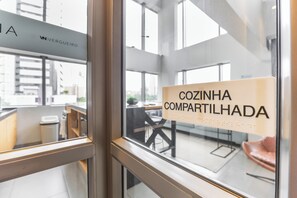 Una ventana con un cartel que dice 'COZINHA COMPARTILHADA' y un vistazo a un espacio de oficina con un escritorio y una silla.