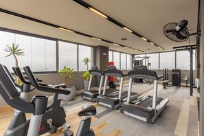 Een sportschool met loopbanden, hometrainers en gewichten, grote ramen en uitzicht over de stad.