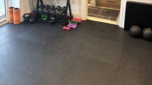 A home gym with exercise equipment, a door leading to a kitchen, and a large window.