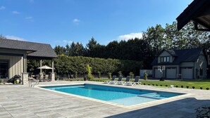 A rectangular swimming pool with a tiled deck, surrounded by lounge chairs and a covered patio area.