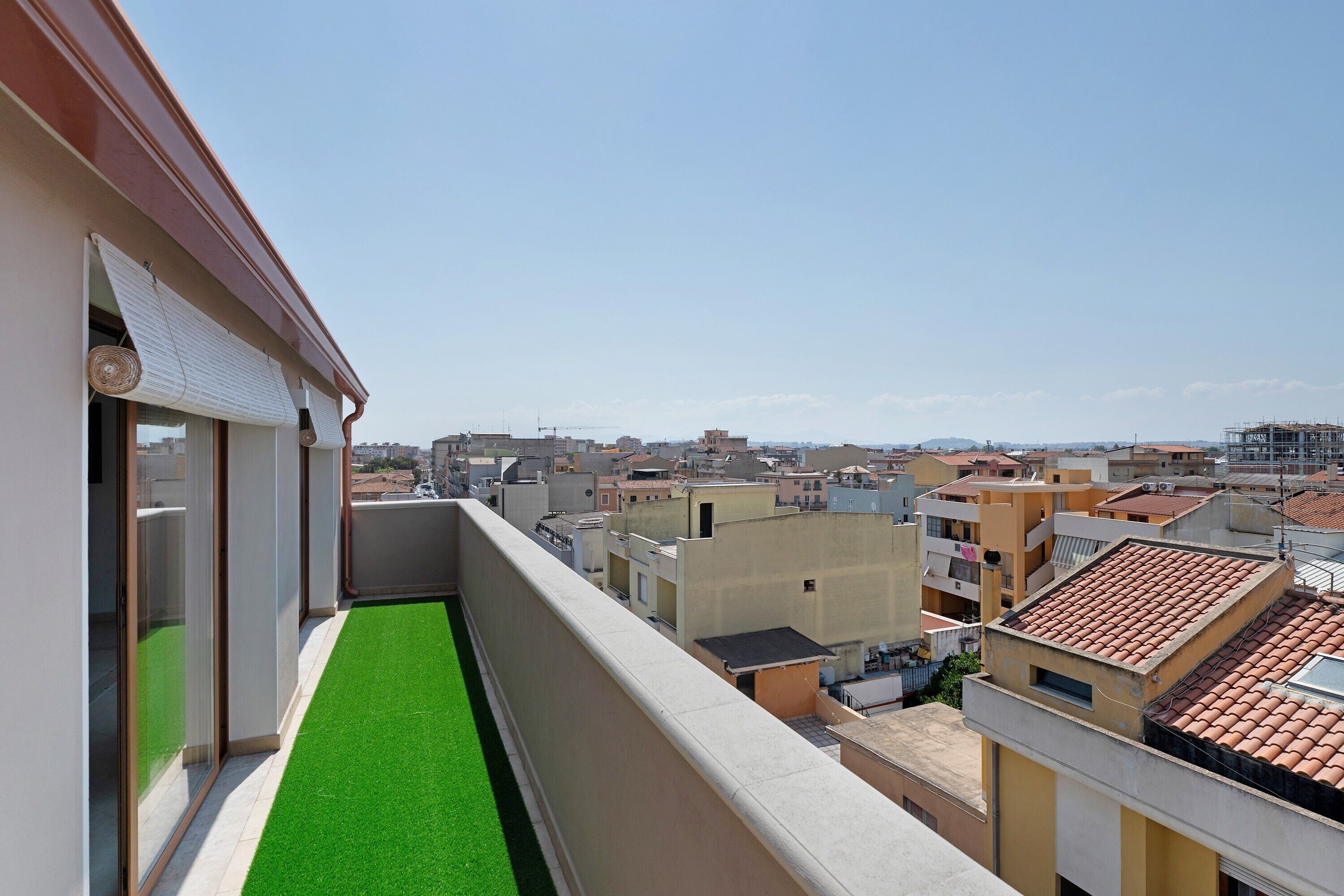 A balcony with a green artificial turf, overlooking a densely packed urban area with various buildings.