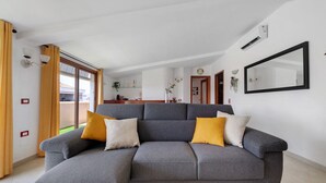 A modern living room with a grey sectional sofa, a black rug, and a large mirror on the wall. - AgoRattico – Elegant Penthouse with Panoramic Terrace (Quartu Sant'Elena)